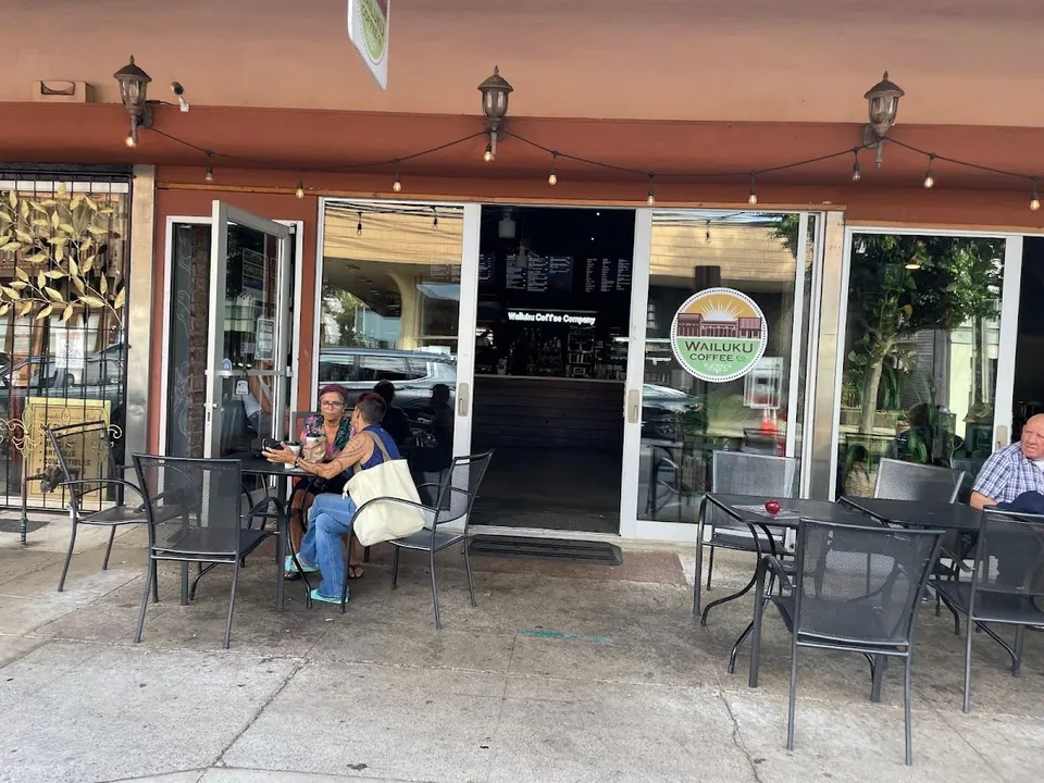 Storefront of Wailuku Coffee Company with string lights, open doors, and people seated at outdoor tables.