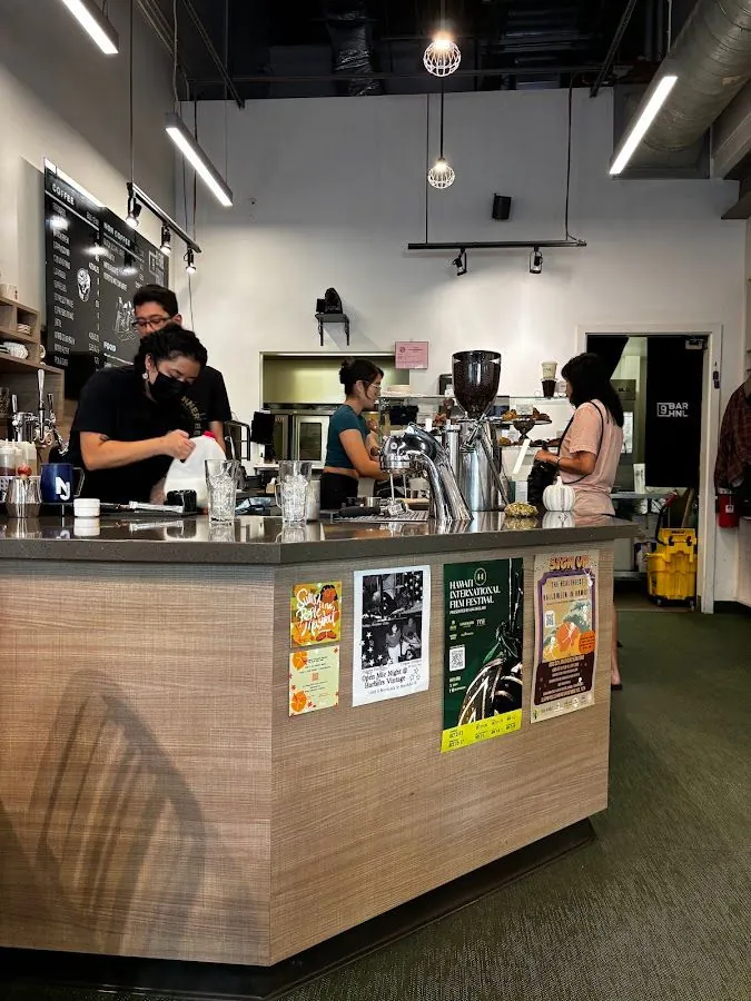 Cafe service counter with staff working, a chalkboard menu, espresso equipment, and event posters on the front.