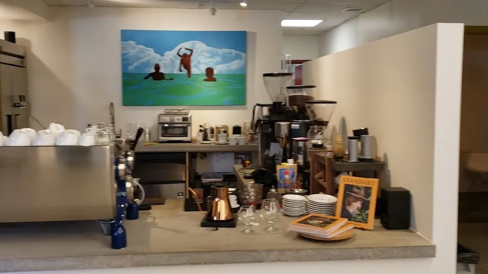 Coffee bar with an espresso machine, grinders, stacked cups, a copper kettle, and a wall painting.