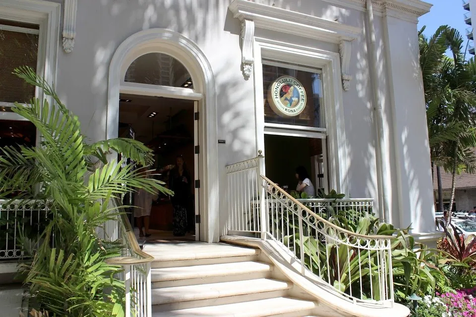 Curved stairs rise to a white arched shop entrance beside a window with a Honolulu Coffee sign.