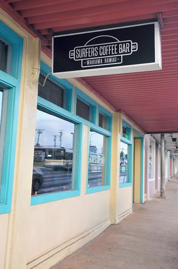 Hanging black sign reading Surfers Coffee Bar, Wahiawa Hawaii, on a covered storefront with turquoise window frames.