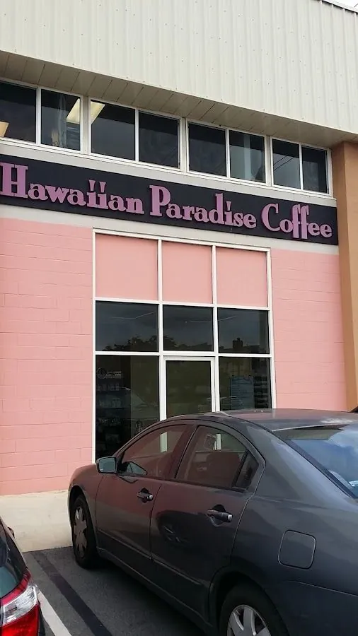 Salmon-pink storefront with a Hawaiian Paradise Coffee sign, large grid windows, and parked cars in front.