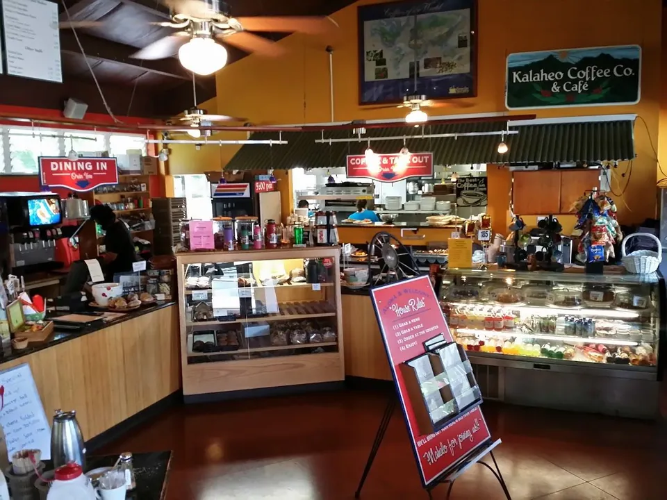 Cafe service counter with pastry cases, order signs, and staff working under orange walls.