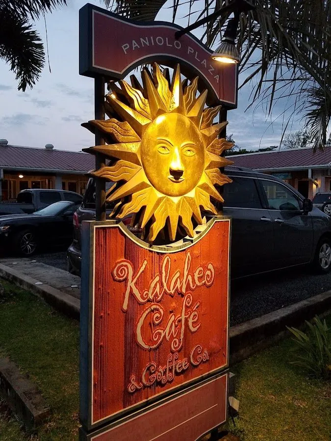 Outdoor sign reading Kalaheo Café & Coffee Co. beneath a lit golden sun at Paniolo Plaza.