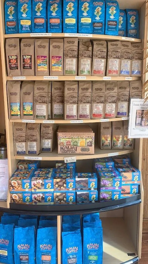 Wooden shelves hold rows of Kauai Coffee bags and blue gift boxes, with price tags and a reserve special sign.