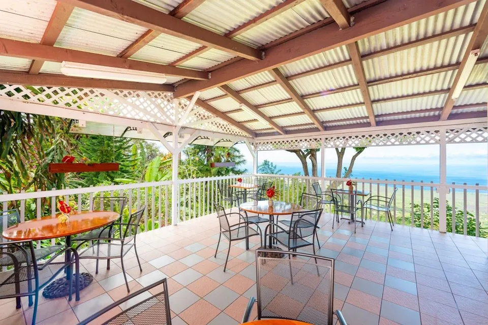 Covered open-air patio with round tables, metal chairs, a tiled floor, and an ocean view.