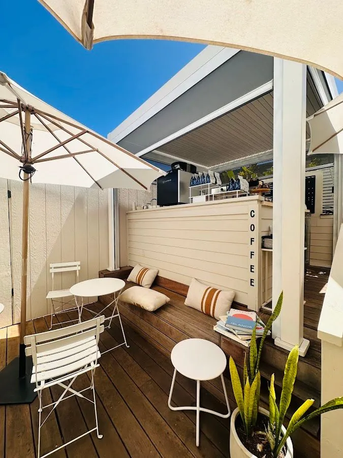 Outdoor wooden deck with white umbrellas, chairs, a cushioned bench, and a vertical COFFEE sign.