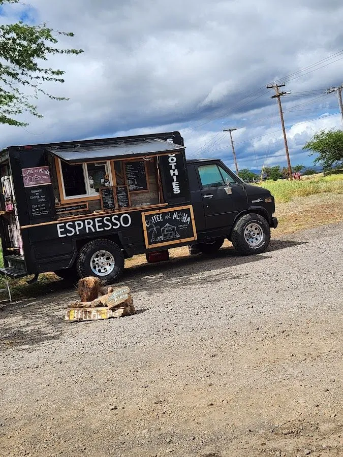 Black coffee truck lettered ESPRESSO and SMOOTHIES, parked on gravel under cloudy skies.