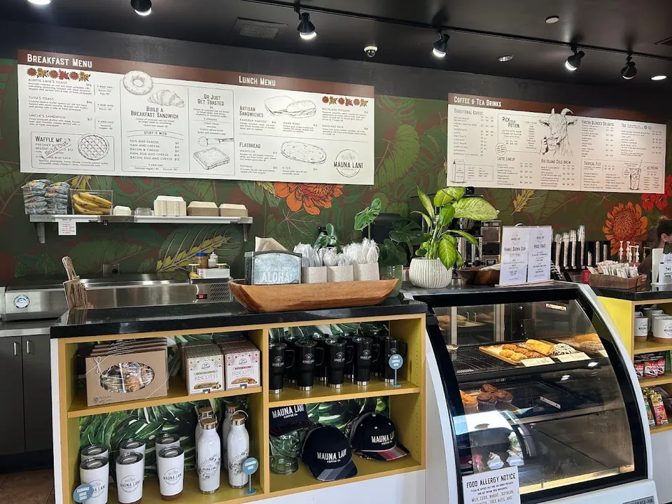 Cafe counter with breakfast, lunch, and drink menu boards, retail shelves, and a pastry case.