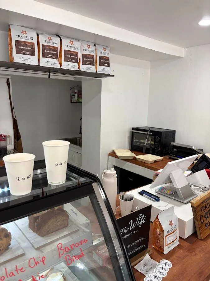 Cafe counter with Tradition Espresso bags on a shelf, labeled hot cups, a pastry case, and a wifi sign.
