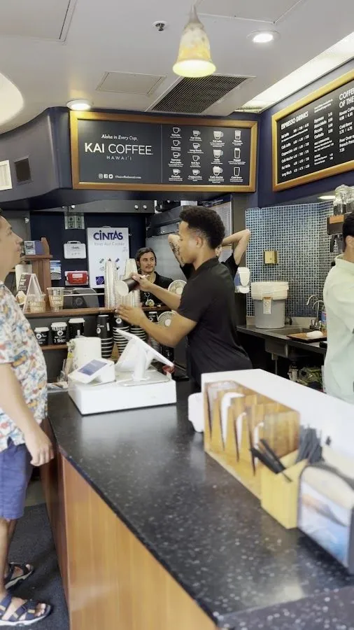 Staff work behind the counter at Kai Coffee Hawaii while a customer waits.