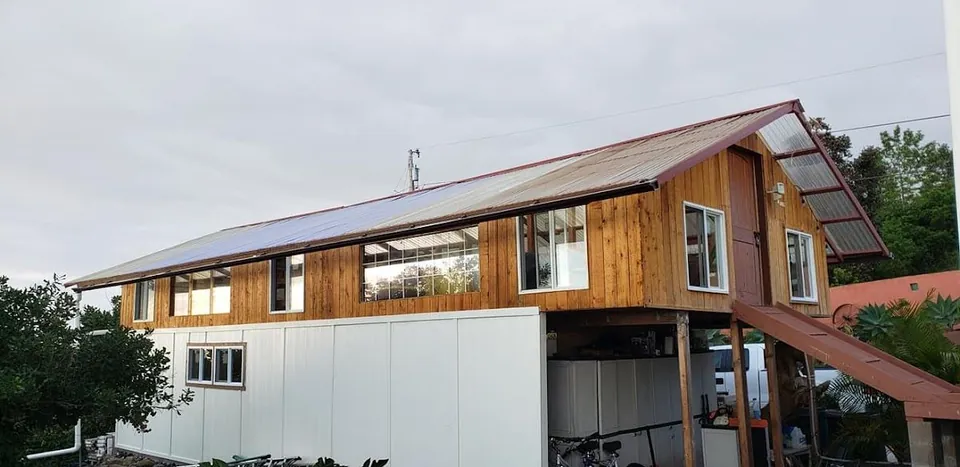 Wooden building with a metal roof, white lower walls, windows, and an entry ramp under a cloudy sky.