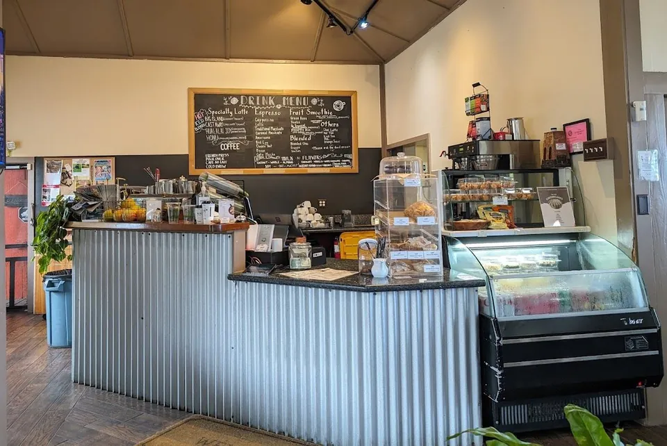 Cafe service counter with a chalkboard drink menu, pastry case, and refrigerated display.
