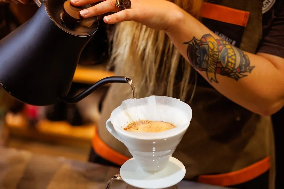 A barista pours water from a kettle into a pour-over dripper at Tradition Coffee Roasters.