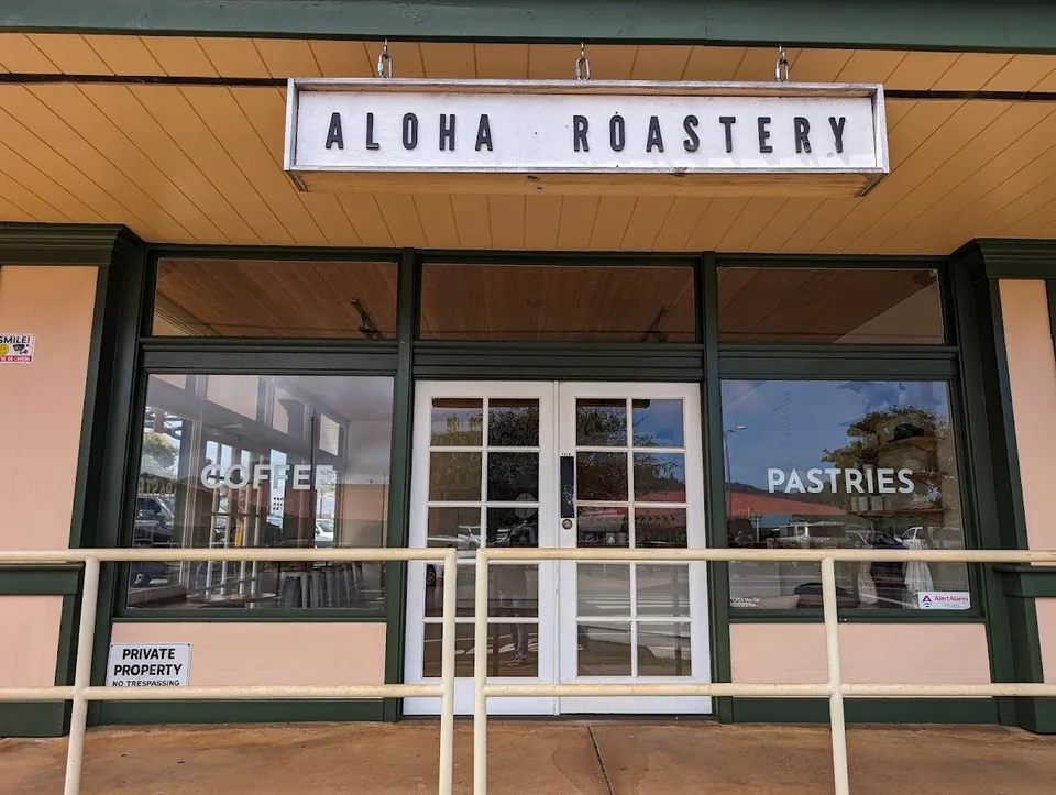 Aloha Roastery storefront with a hanging sign, coffee and pastries lettering on the windows, and white double doors.