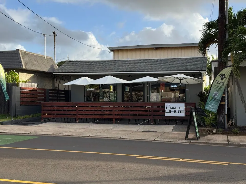 Single-story shop on a street with white umbrellas, a wooden patio rail, and Hale Lihue and Ha Coffee signs.