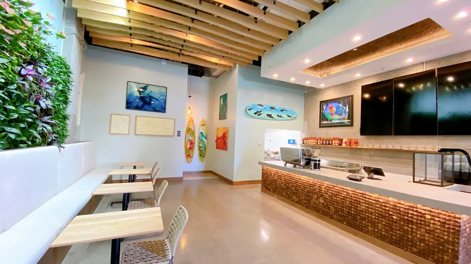 Cafe seating with white benches and wood tables beside a wood-fronted service counter and espresso machine.