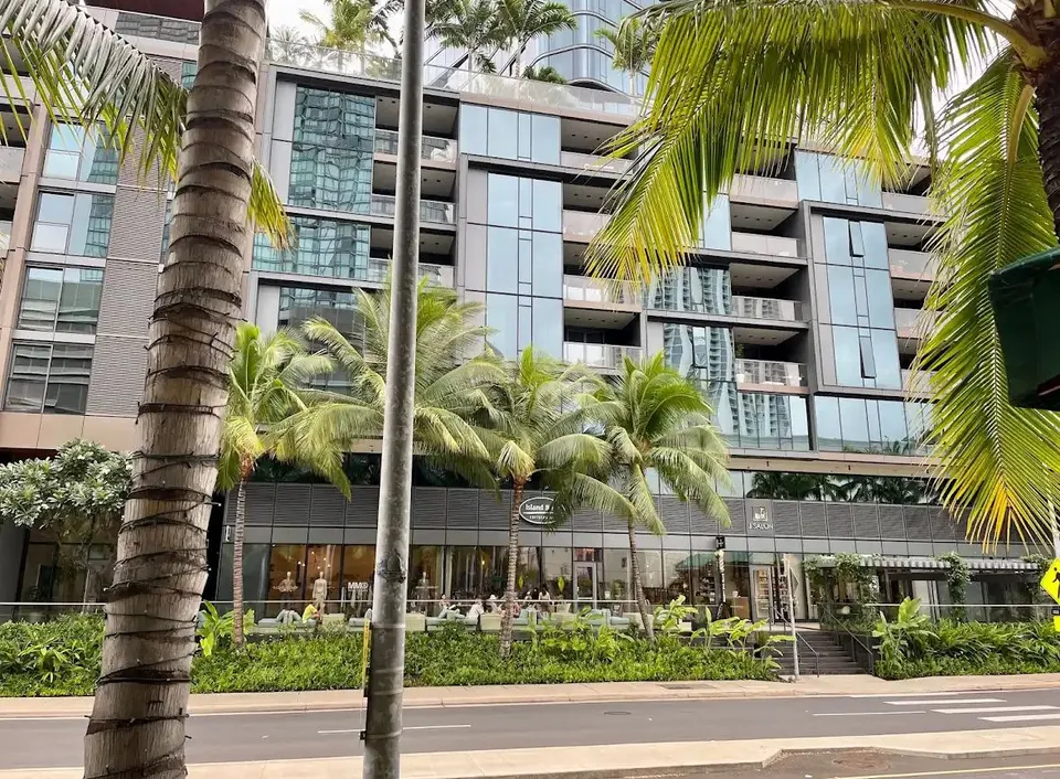 Glass high-rise behind palms, with people seated at street-level tables and shop signs.