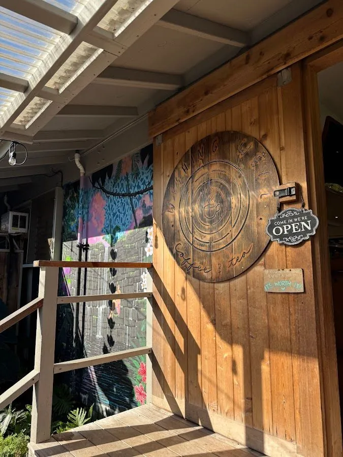 Wooden shop entrance with a round Wishing Well Coffee & Tea sign, an open sign, and a floral mural.