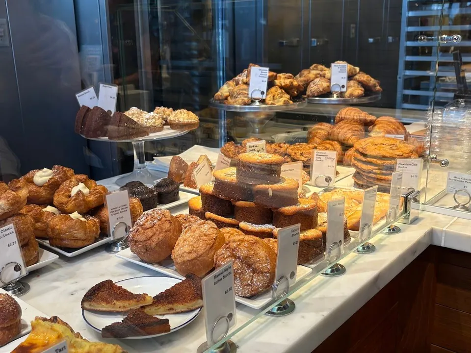 Glass pastry case on a marble counter, filled with cakes, cookies, and price cards.