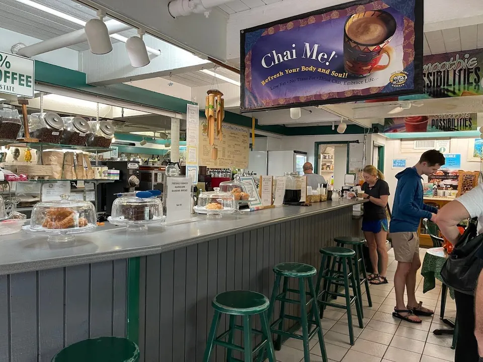 Counter with green stools and covered baked goods; one person works behind it while others stand nearby.