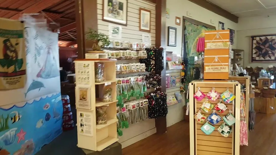 Shop interior with merchandise racks, hanging cards and beads, fabric goods, and an E Komo Mai welcome box.