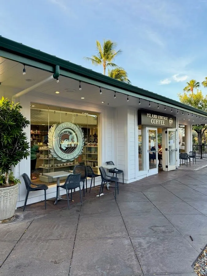 Island Vintage Coffee storefront with white walls, green roof, patio tables and chairs, and palm trees.