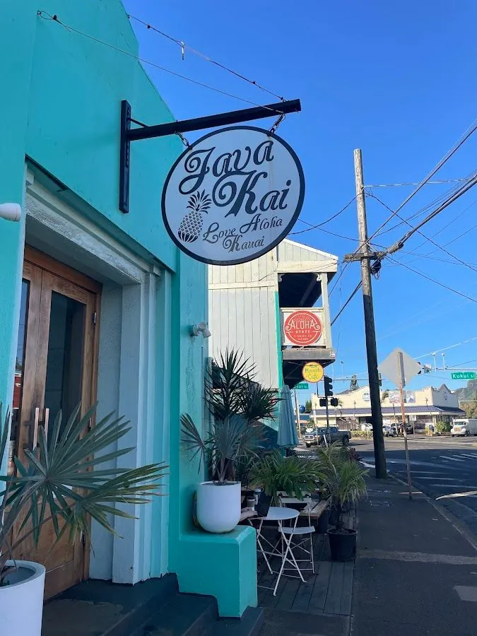 Round Java Kai sign hangs from a turquoise storefront beside a wooden door and sidewalk tables.