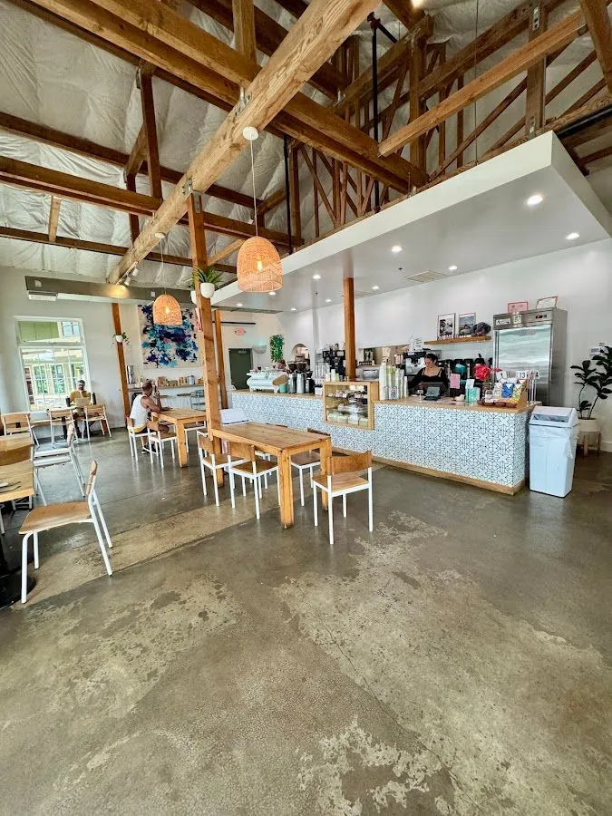 Cafe interior with seated customers, a staffed tile counter, wood tables, and exposed ceiling beams.