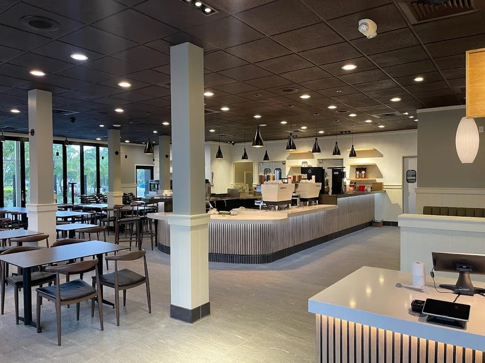 Cafe dining room with tables, chairs, a long service counter, espresso machines, and hanging lights.
