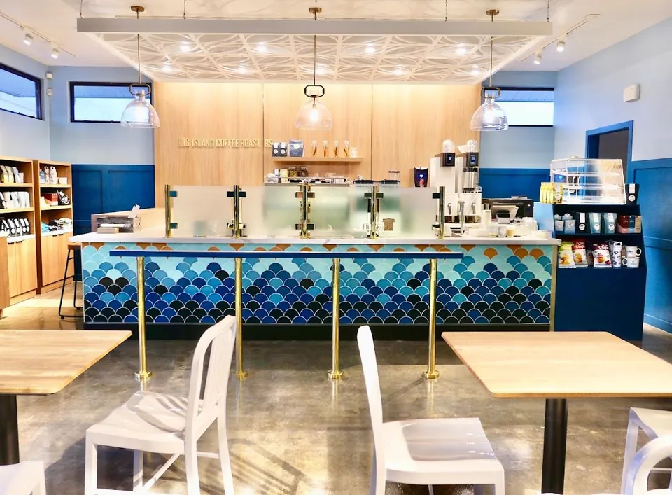 Service counter with blue scalloped tiles, brass posts, pendant lights, wood tables, and white chairs.