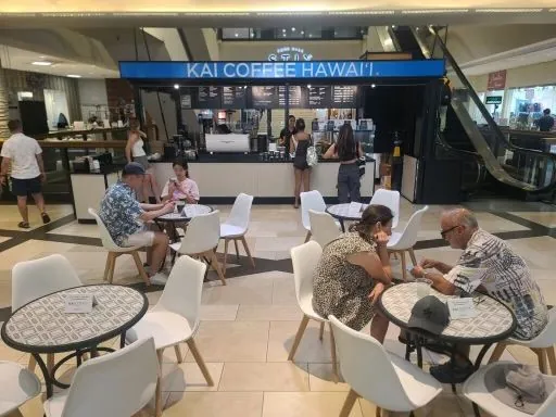 Mall seating area in front of a Kai Coffee Hawai'i counter, with people at tables and the service counter.