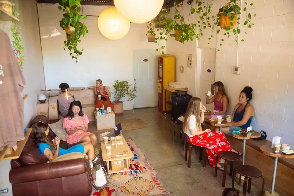 Seating area with leather sofa, wood tables, hanging plants, paper lanterns, and people holding cups.