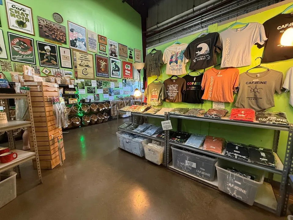 Lime-green shop interior with coffee posters, hanging printed shirts, mugs, and folded apparel on shelves.
